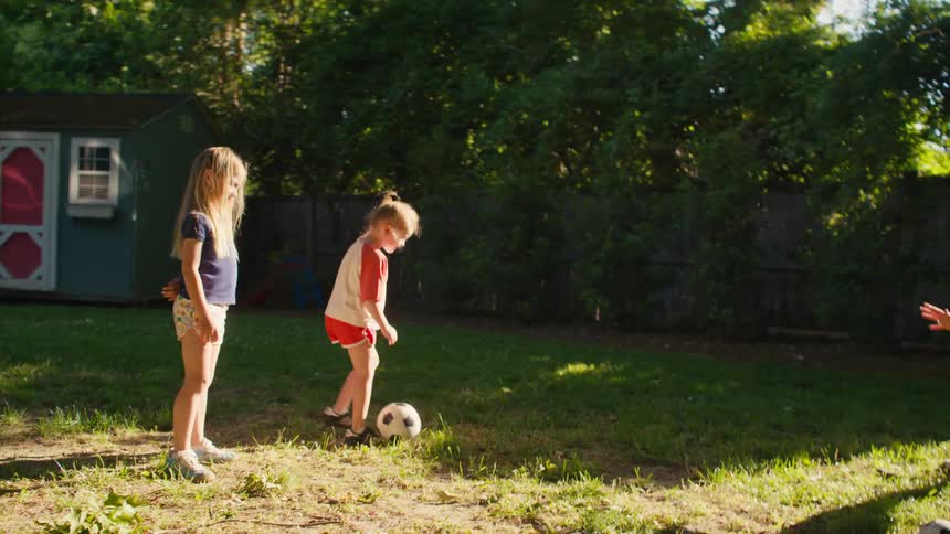 A young girl scores a soccer goal in the backyard against her mom and joyfully celebrates with her sister