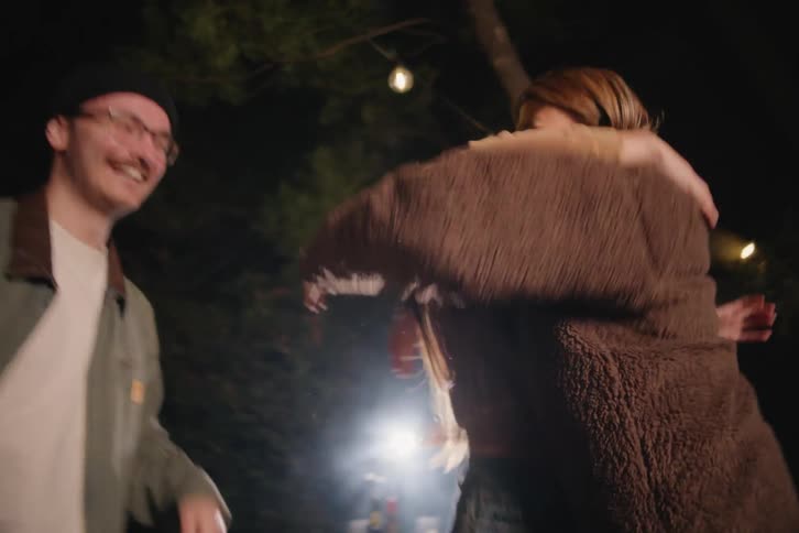 A group of ecstatic friends leap from their outdoor couch in slow motion to celebrate a thrilling moment while watching a game at night