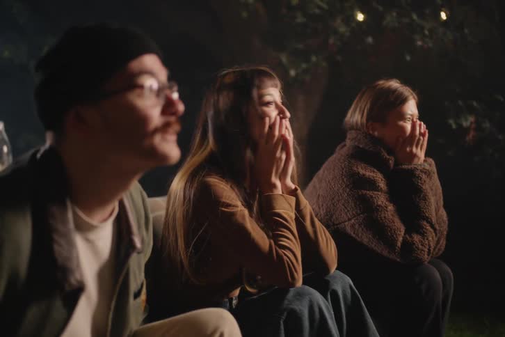 A group of friends gets a fright while watching a scary movie outdoors at night, causing them to spill the popcorn in shock