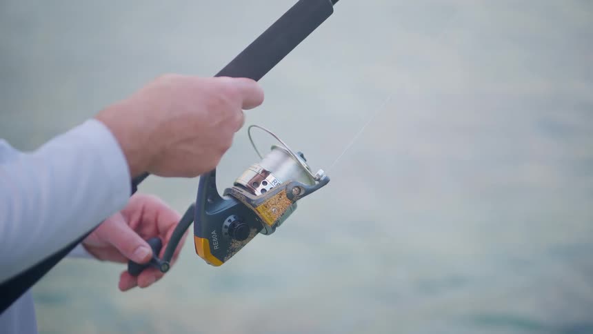 A close-up shot of a fisherman's hands as he reels in the line on his fishing rod over calm water