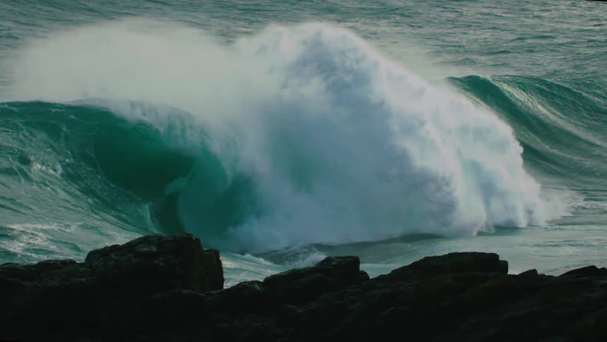 A powerful teal ocean wave crests and crashes in dramatic super slow motion
