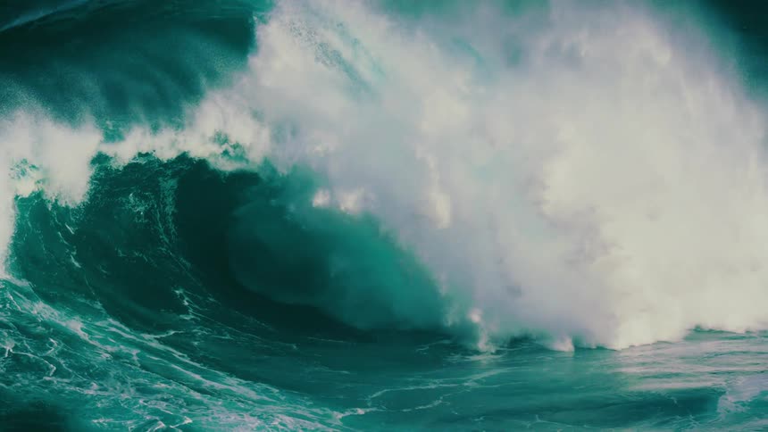A giant, powerful turquoise ocean wave curls and breaks in a dramatic slow motion display of raw natural force