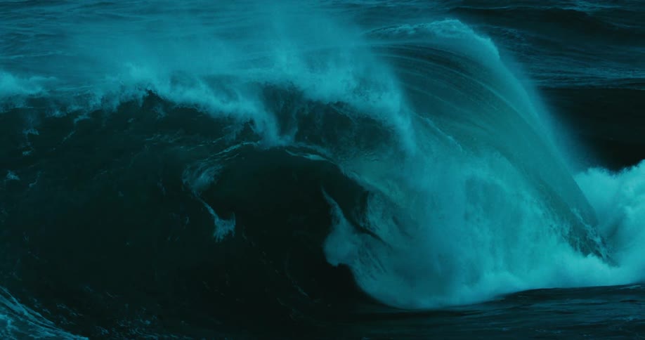A massive teal ocean wave curls and breaks in dramatic slow motion
