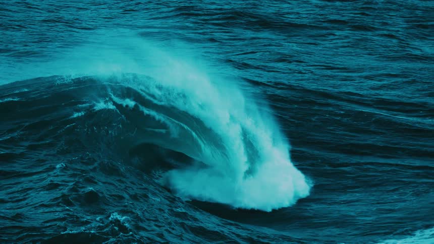 A majestic, dark teal ocean wave curls and crashes in mesmerizing slow motion