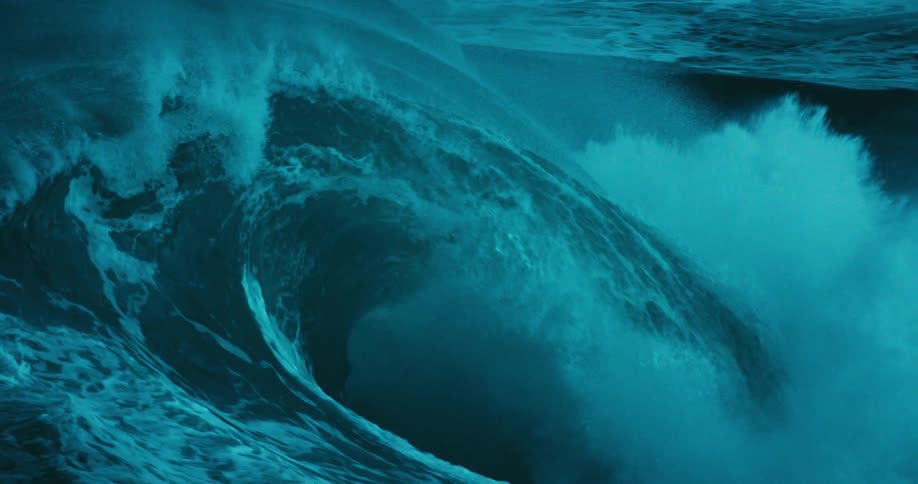 A mesmerizing close-up of a massive, dark blue ocean wave cresting and breaking in dramatic slow motion