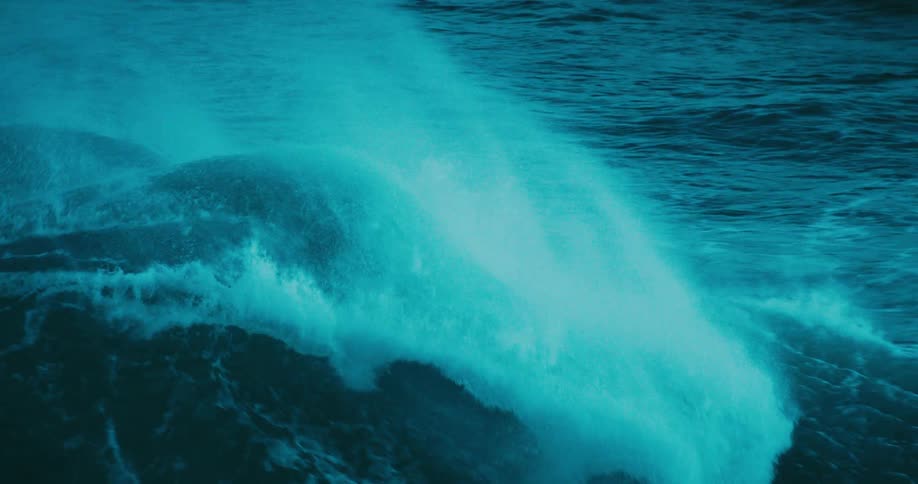 A powerful, dark turquoise ocean wave crests and breaks in mesmerizing super slow motion