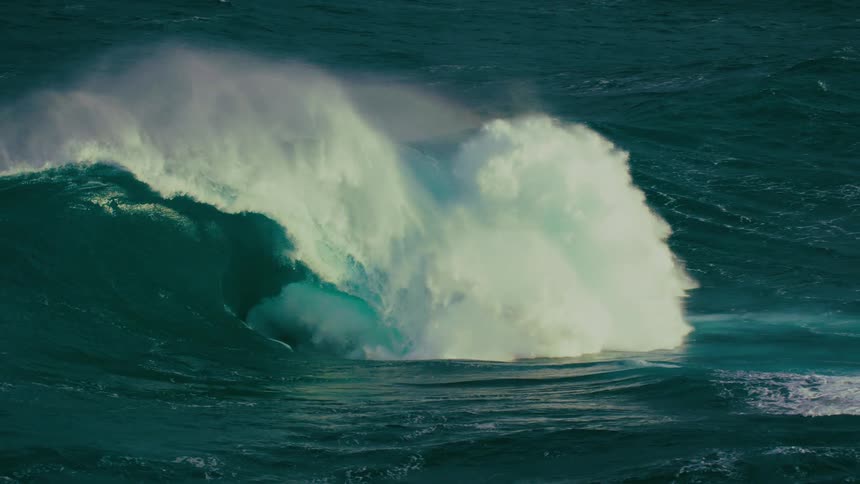 A powerful, backlit ocean wave builds and crashes in dramatic slow motion