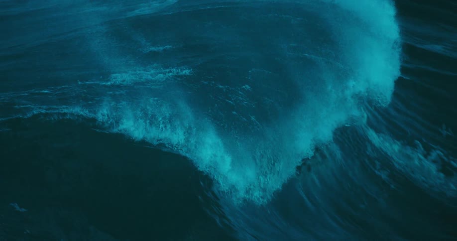 A powerful, dark blue ocean wave builds and crests in dramatic slow motion