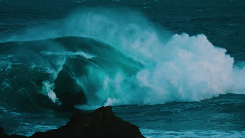 A massive turquoise ocean wave curls and crashes with immense power in dramatic slow motion