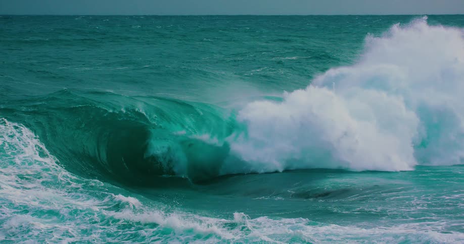 A powerful turquoise ocean wave curls and crashes in dramatic slow motion
