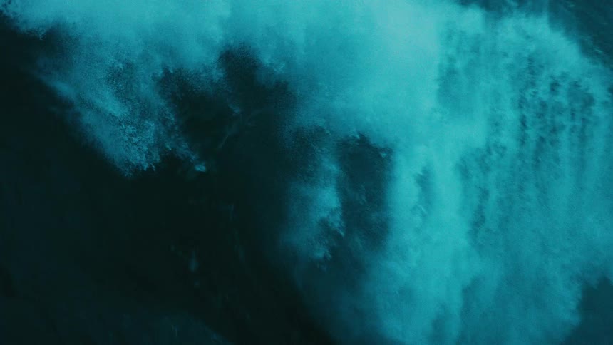 A powerful turquoise ocean wave builds and crashes in dramatic, mesmerizing slow motion