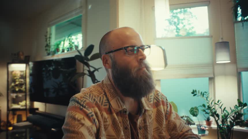 A man with a beard and glasses closes his laptop, finishing his work from home in a cozy living room