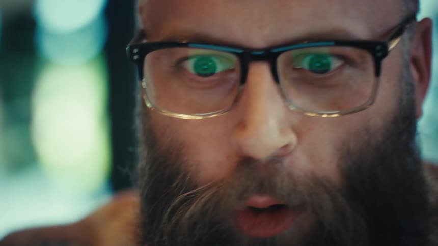 Close-up of an animated bearded man with glasses getting excited and leaning into his laptop screen during a video call