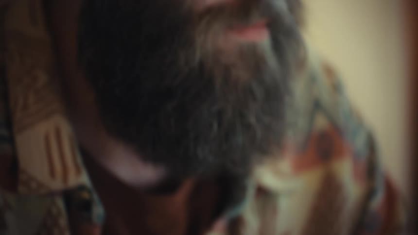 Close up of a bearded man with glasses working intently on his laptop in a warmly lit room