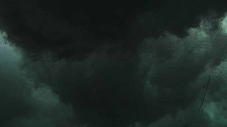 A dark, eerie underwater view looking up at the churning and turbulent surface of the ocean