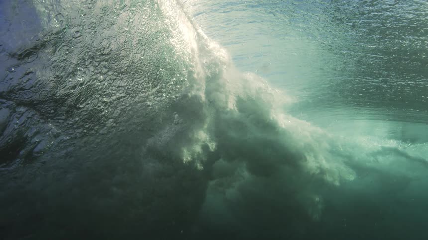 An incredible underwater slow-motion view of a powerful ocean wave breaking as sunlight shines through the water's surface