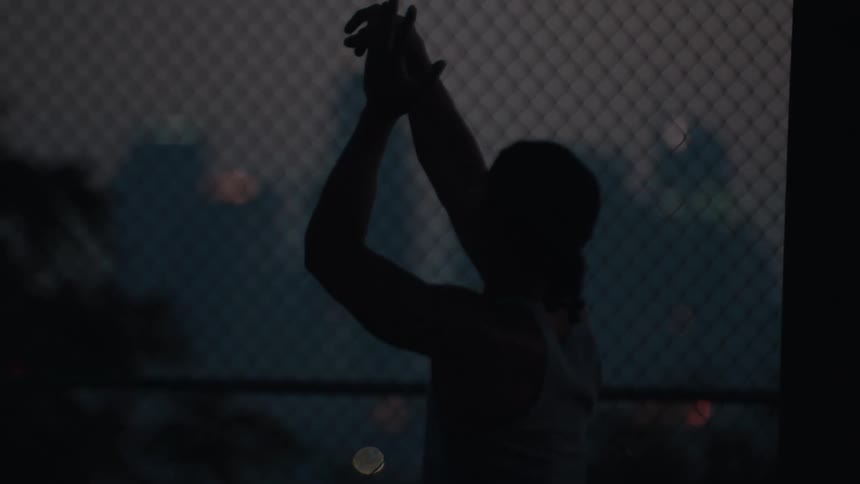 Slow-motion silhouette of a person taking a jump shot on an urban basketball court at night