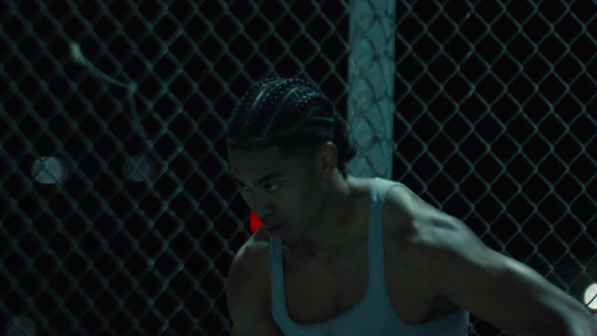 A serious and muscular basketball player contemplates his next move on a dimly lit city court in slow motion