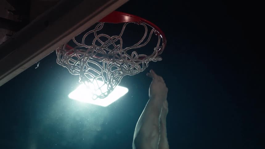 Cinematic slow motion shot of a basketball player executing a powerful slam dunk at night under a single spotlight