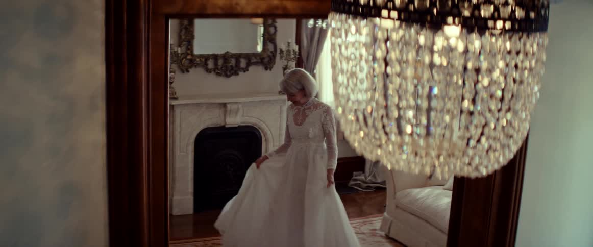 A graceful senior bride in a beautiful white wedding gown twirls in slow motion in an elegant, vintage room with a crystal chandelier