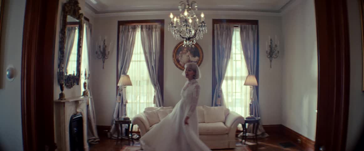 A dramatic woman in a vintage white gown sings and twirls slowly in an ornate living room