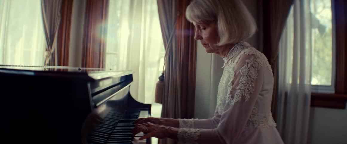An elegant elderly woman in a beautiful white lace dress plays the piano in a sunlit room