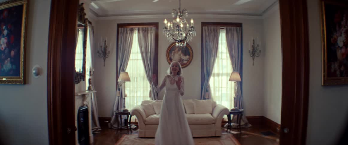An elegant elderly woman in a beautiful wedding gown dreamily dances and twirls alone in a grand, sunlit living room