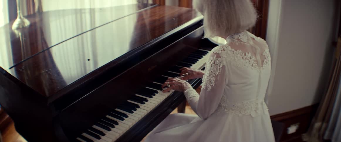 An elegant senior woman wearing a white lace dress gracefully plays a classical piano in a sunlit room