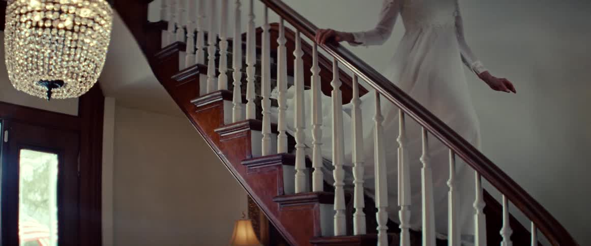 An elegant older bride in a white lace wedding gown gracefully descends a grand wooden staircase