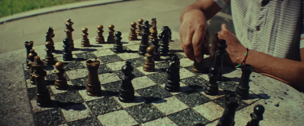 A close-up of two people playing a game of chess on a stone table in a park