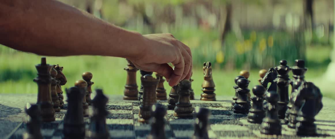 A person makes a strategic chess move with a wooden piece on a stone board outdoors in a sunny park