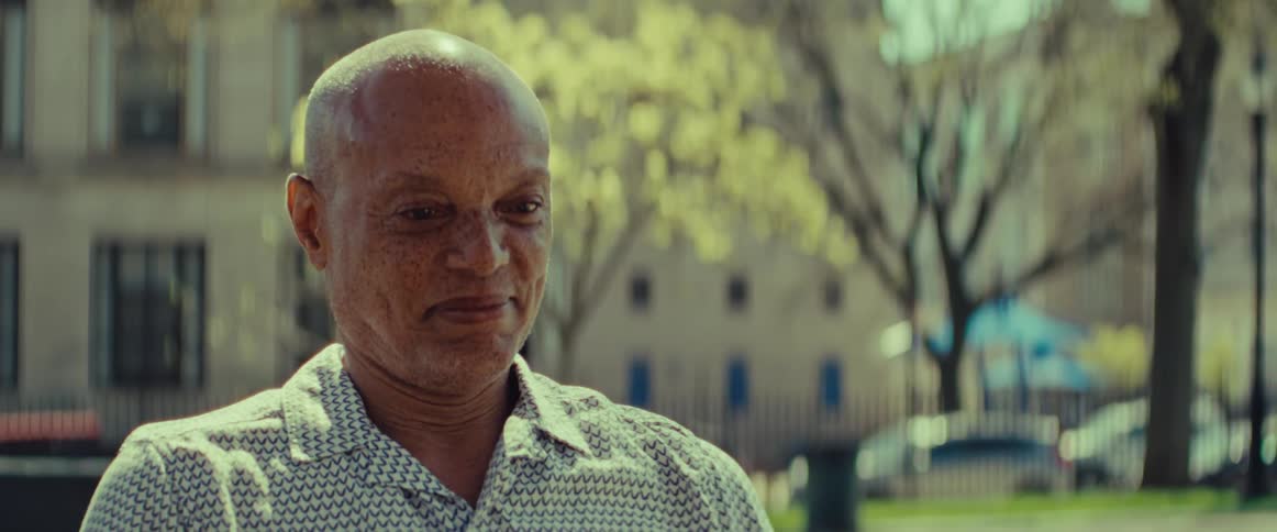 A serene older man smiles gently while enjoying the warm sunshine in a city park