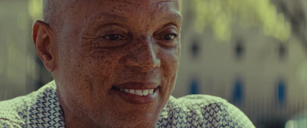 An intimate close-up of a senior man with a kind and warm smile on his face, enjoying a sunny day outdoors