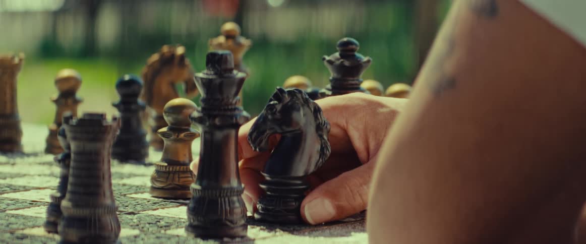Close-up on a chess player's hand contemplating a move with the black knight on a park chessboard