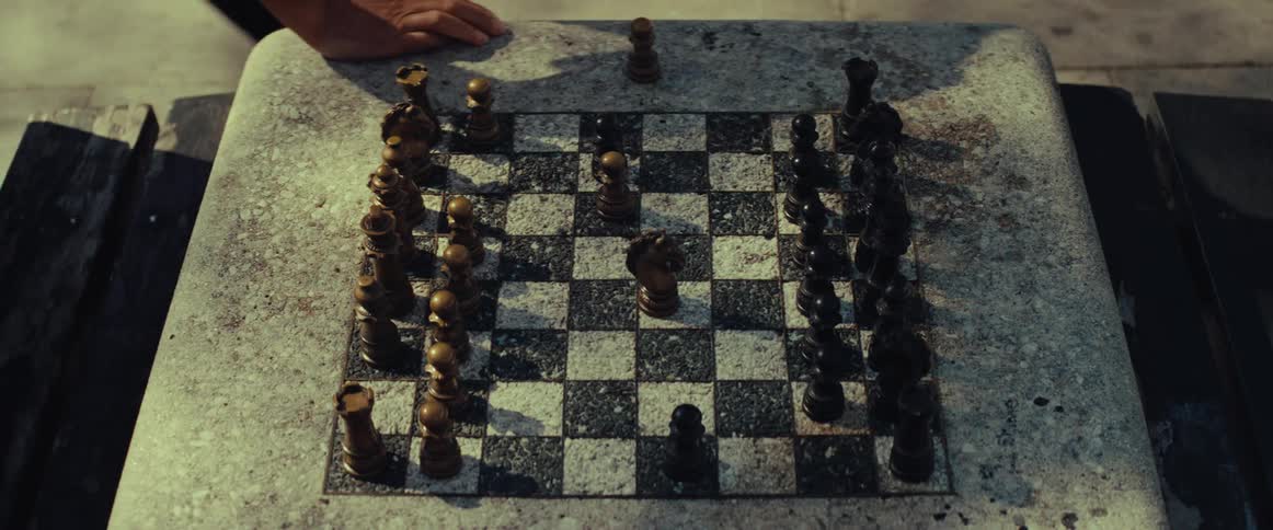 An overhead view captures two players making strategic moves during a chess match on a stone table