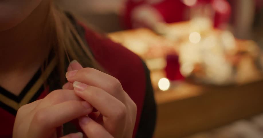 Close-up shot of a young person's hands nervously playing with a strand of their hair in a warm, intimate setting