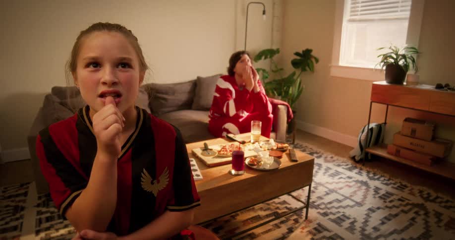 A young girl and her father react with disappointment while watching a sports game in their living room