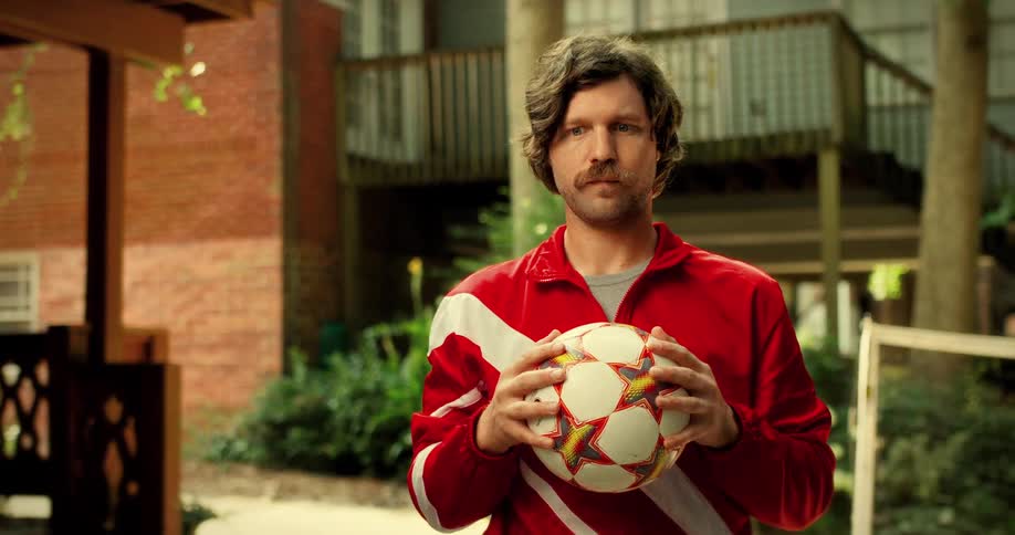 A cinemagraph portrait of a retro 80s soccer player with a mustache and red tracksuit tossing a soccer ball
