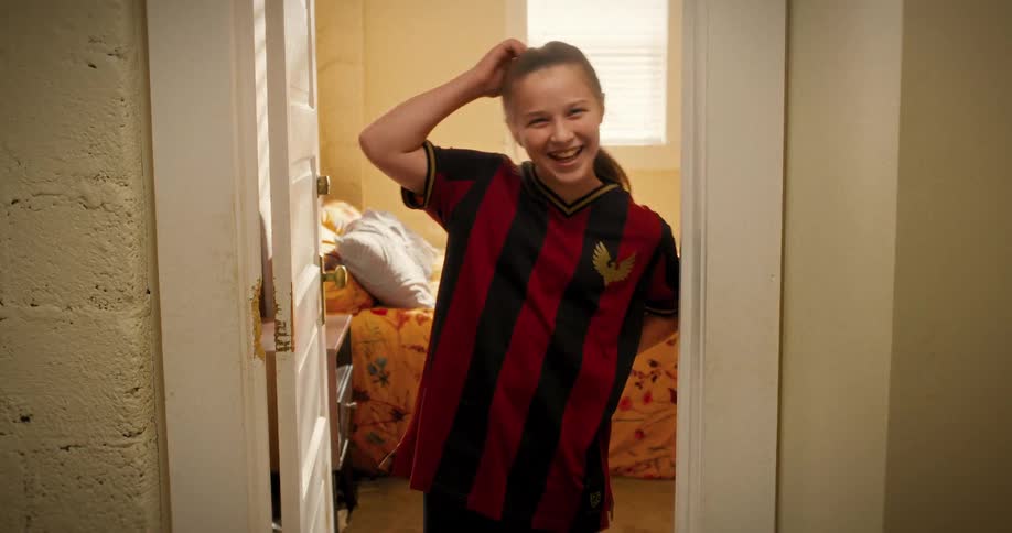 A smiling young female soccer player poses playfully in the doorway of her room