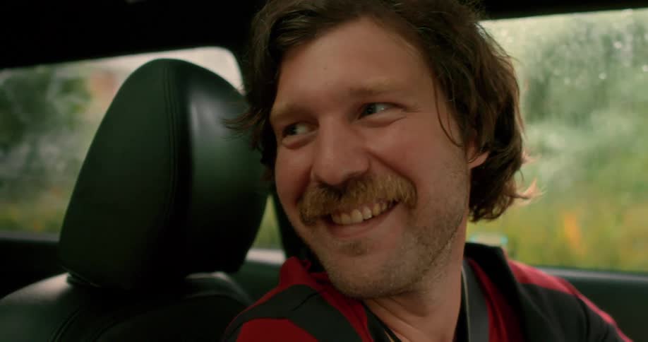 Close-up of a happy man with a mustache laughing while riding in a car on a rainy day