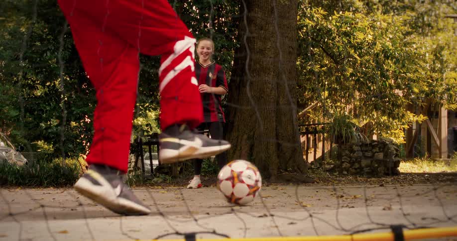 Super slow motion shot of a soccer ball being kicked into the net as a young girl and her coach practice in the park