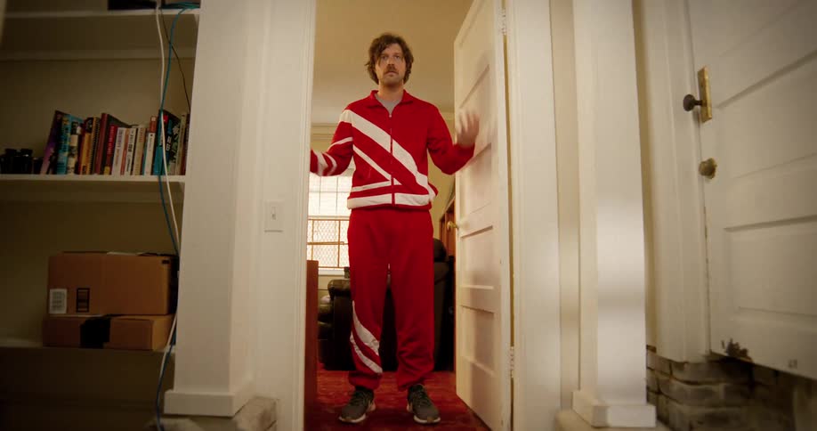 A quirky man in a vintage red tracksuit makes a grand entrance into a hallway