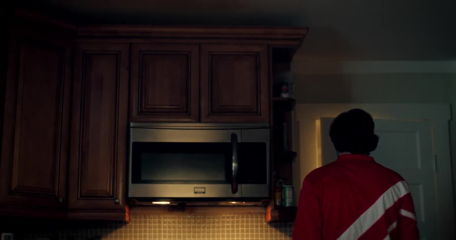 A disheartened man with a mustache, wearing a retro red tracksuit, sighs with disappointment in his kitchen before walking away