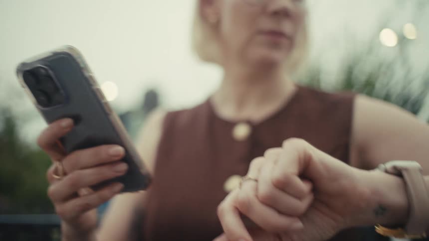 A close-up shot racks focus from a woman's hands on her smartphone to her smartwatch on her wrist