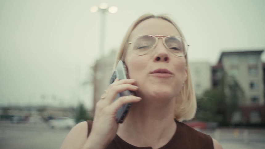 A businesswoman experiences a rollercoaster of emotions from joy to anger while having an intense conversation on her phone outdoors