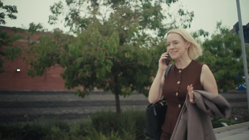 A businesswoman happily laughs while talking on her phone and walking through the city in slow motion