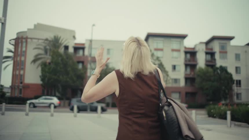 A successful businesswoman with blonde hair celebrates a victory over the phone while walking through a city plaza in slow motion