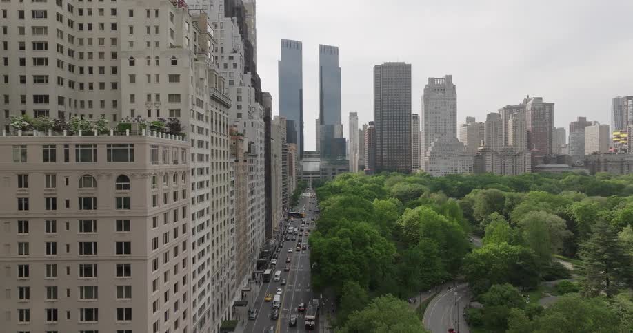 An aerial drone slowly flies along the edge of Central Park, revealing the iconic Manhattan skyline and the contrast between urban and natural landscapes