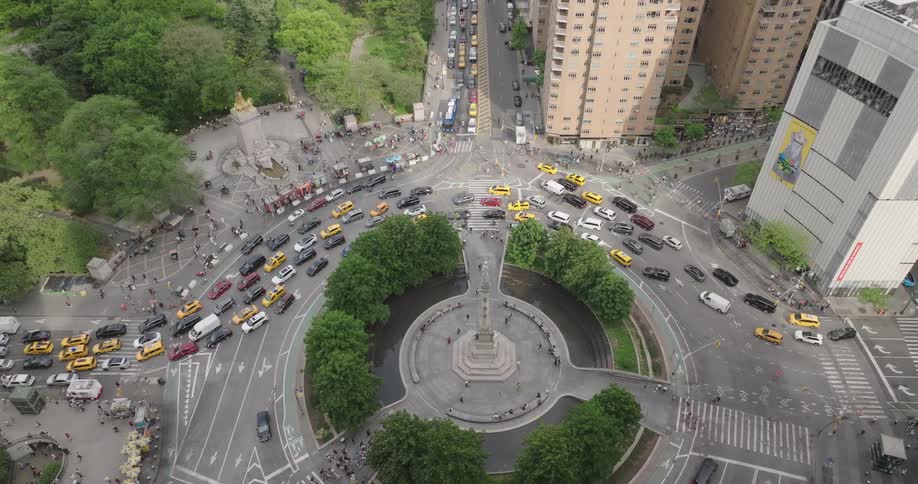Aerial drone shot tilts down from between two skyscrapers to reveal the busy traffic of Columbus Circle next to Central Park in New York City