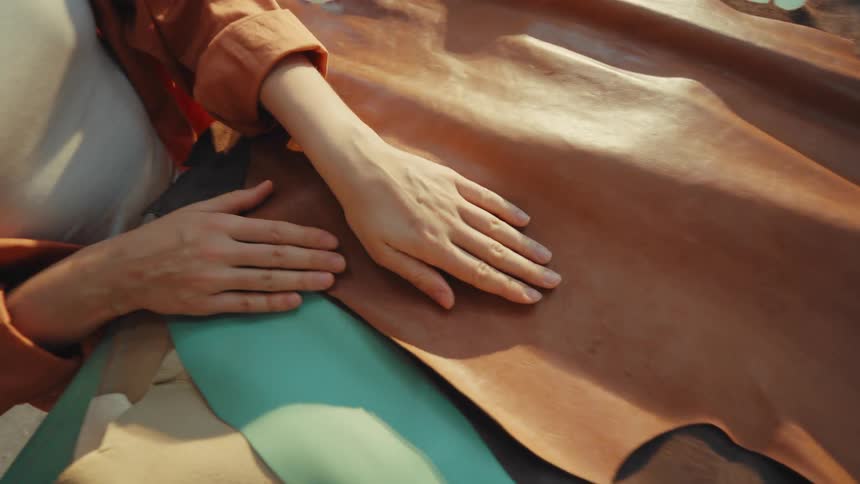 Top-down view of a designer's hands touching and stroking a piece of natural brown leather hide